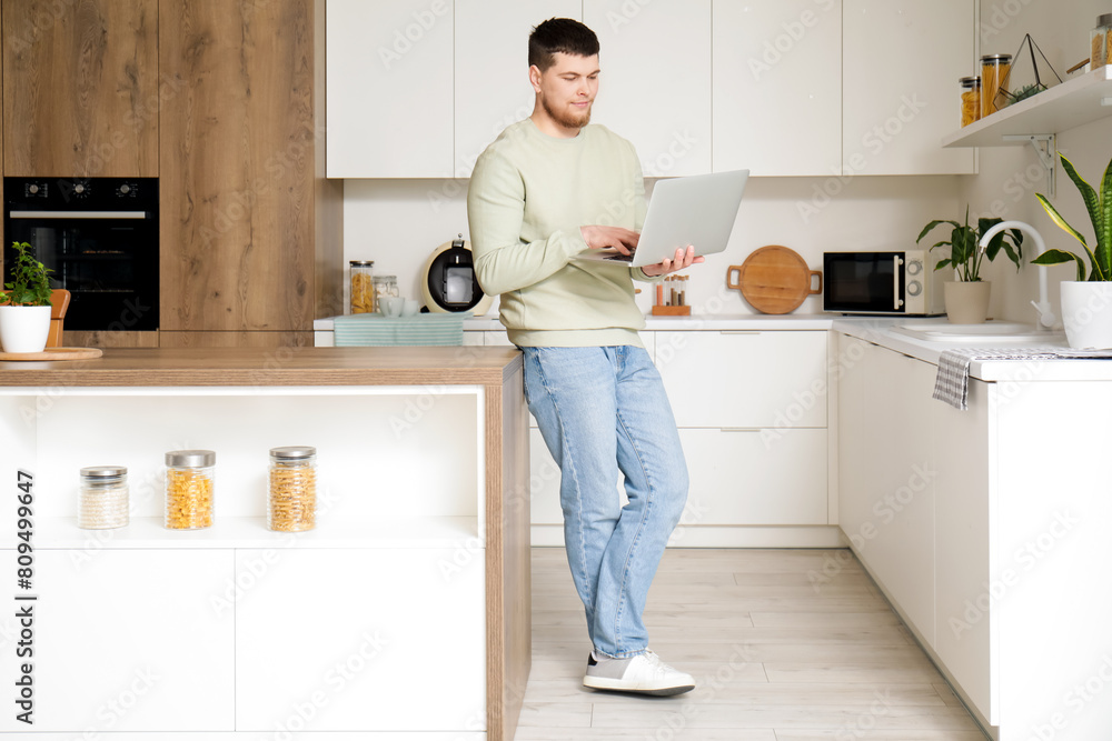 Young bearded man using laptop in kitchen Young bearded man using laptop in kitchen