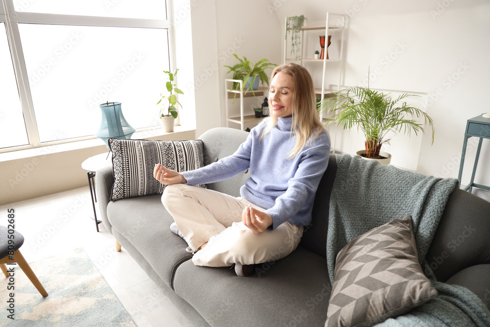 Young woman meditating on sofa in white living room Young woman meditating on sofa in white living room