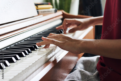 Hands of woman playing grand piano in musical school.Two hand with different level and keyboard.Blur background with light.Female pianist hands on grand piano keyboard.Playing music or song at home.