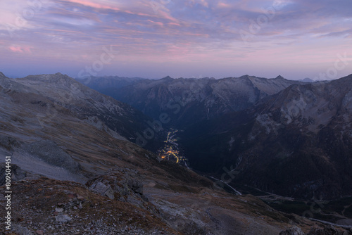 Aerial view at dusk of an Alpine valley with the lights of a mountain village. Macugnaga and the Anzasca valley at the foot of Monte Rosa seen from the Eugenio Sella bivouac, Piedmont region, Italy