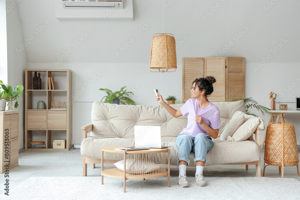 Young African-American woman turning on air conditioner at home Young African-American woman turning on air conditioner at home