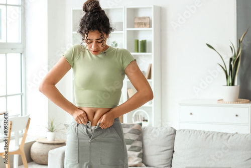 Quadro su tela Young African-American woman trying to button tight skirt at home