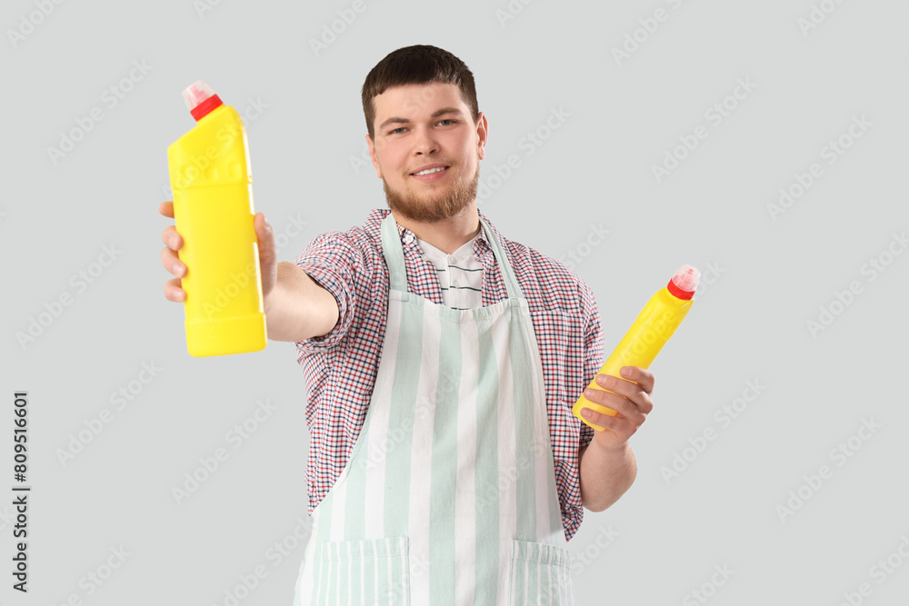 Young bearded man with bottles of detergent on light background Young bearded man with bottles of detergent on light background