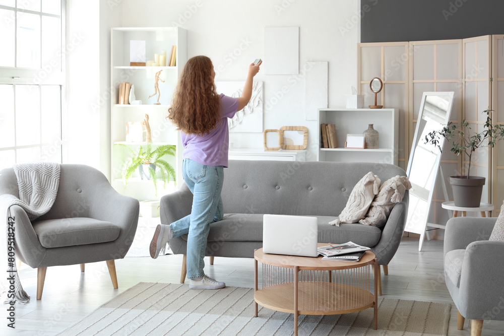 Young woman with air conditioner remote control in living room Young woman with air conditioner remote control in living room