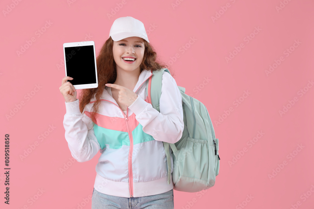 Happy female student with backpack pointing at tablet computer on pink background Happy female student with backpack pointing at tablet computer on pink background