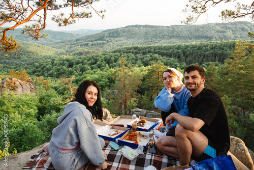 happy friends eating pizza at the cliff with beautiful mountain view