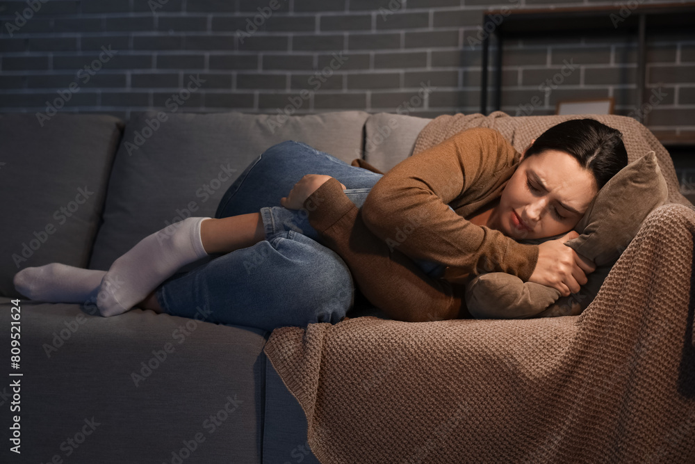 Depressed young woman lying on sofa at home in evening Depressed young woman lying on sofa at home in evening