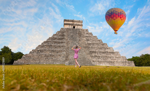 Hot air balloon flying over The pyramid of Kukulcan in the Mexican city of Chichen Itza - Young girl is standing and taking photos in  the background - Mayan pyramids in Yucatan, Mexico photo