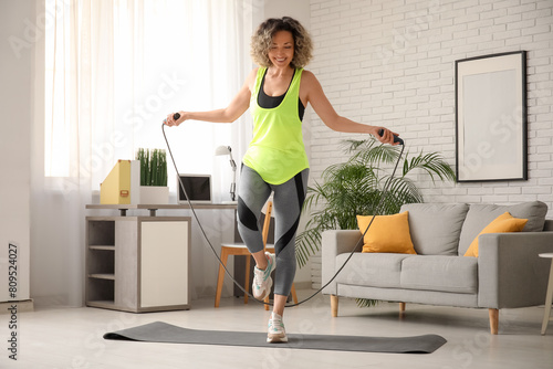 Fotografie Happy mature sporty woman training with jumping rope at home