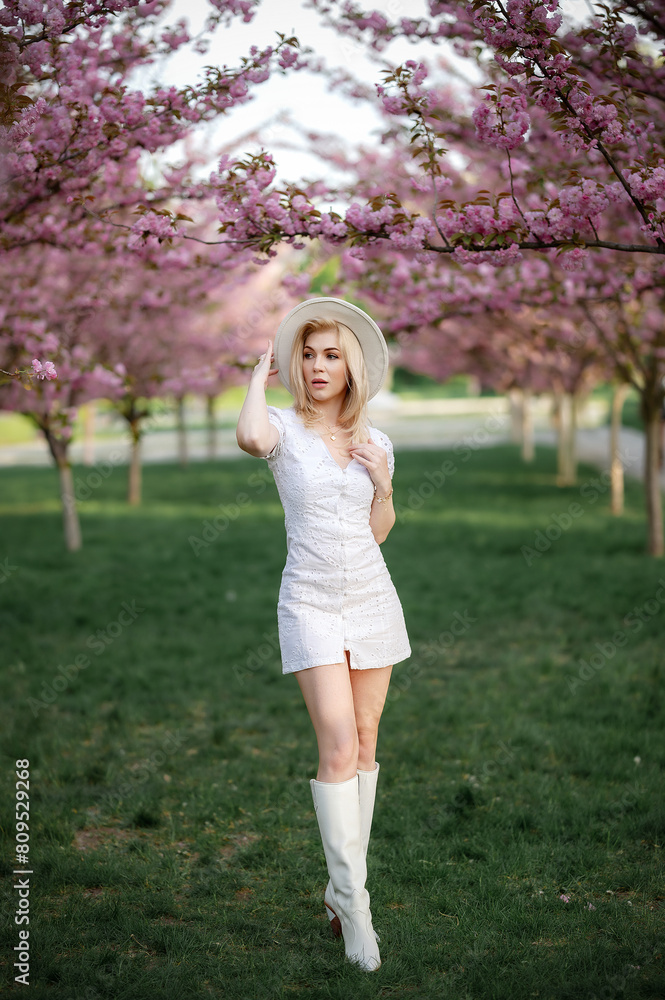 A beautiful blonde stands against the background of flowering trees A beautiful blonde stands against the background of flowering trees