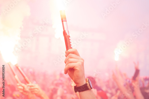 Football fans burning smoke flares, holding red fire torches in hands. Crowd of excited soccer fans showing their support for a favorite team. Ignite stadium flame flare up in the air.