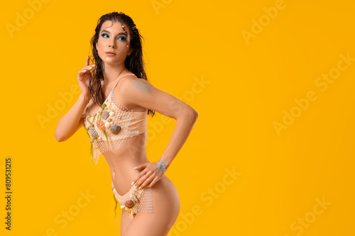 Beautiful young woman dressed as mythical mermaid on yellow background photo