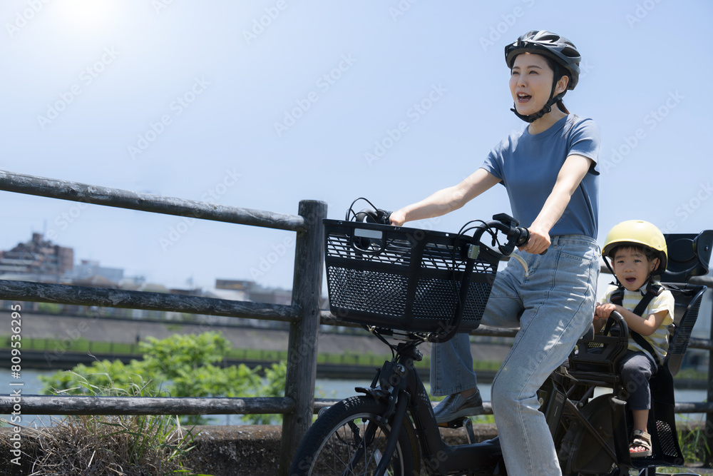 Naklejka premium 青空の綺麗な道を自転車に乗るママと子供 ママチャリでお出かけや出勤