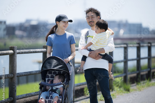 Upper half of a parent and child (family of four) taking a walk in a park along a river in sunny weather Image of spring and summer outings, leisure activities, etc.