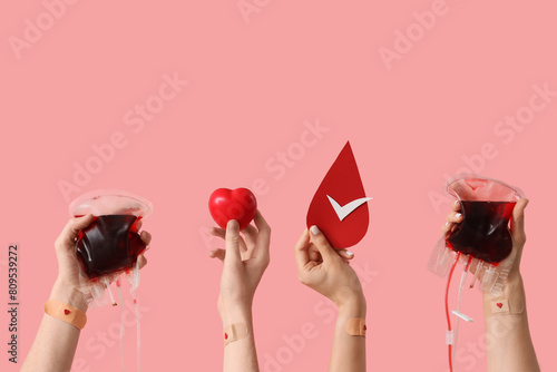 Blood donors with packs for transfusion, grip ball and paper drop on pink background photo