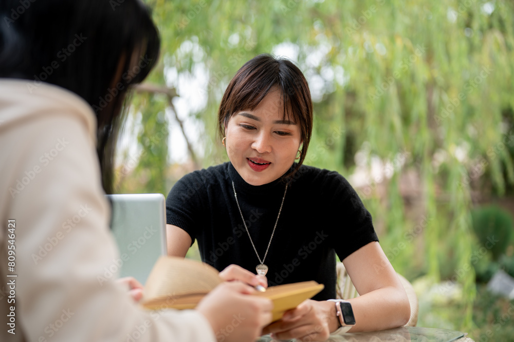 An Asian woman working remotely in a garden with her colleague, explaining some details in the book.