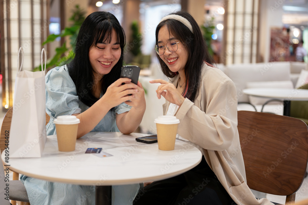 Two Asian female friends are enjoying talking while sitting together in a cafe in the shopping mall.