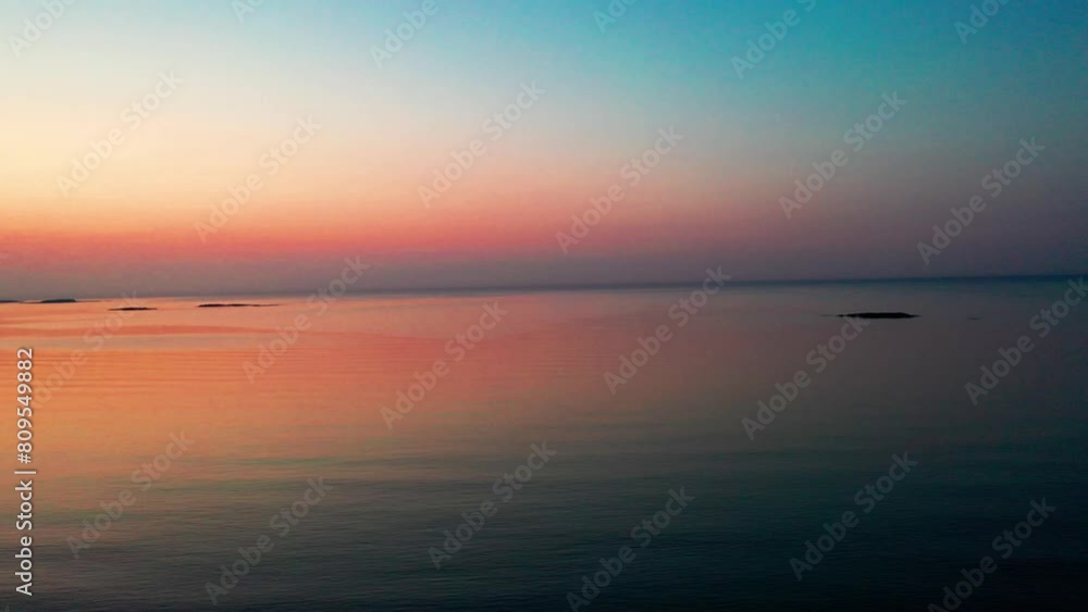 Drone Lowering over Calm Beautiful Ocean Sunrise with Small Islands on the Horizon. Plus Colorful Red and Yellow Reflections on Water. Aerial View of Pristine Sea