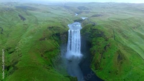 Majestic Aerial view reveals the grand scale of a powerful Skogafoss waterfall flowing through a vast green landscape, with its waters cutting a dramatic path through the terrain. Iceland, Skogar.  photo