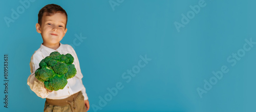 A studio shot of a boy holding fresh broccoli on a blue background with a copy of the space. The concept of healthy baby food. photo