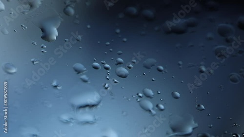 lunga ripresa in tempo reale e con vista macro di gocce di pioggia che si infrangono su un vetro con sfondo sfuocato e color azzurro scuro photo