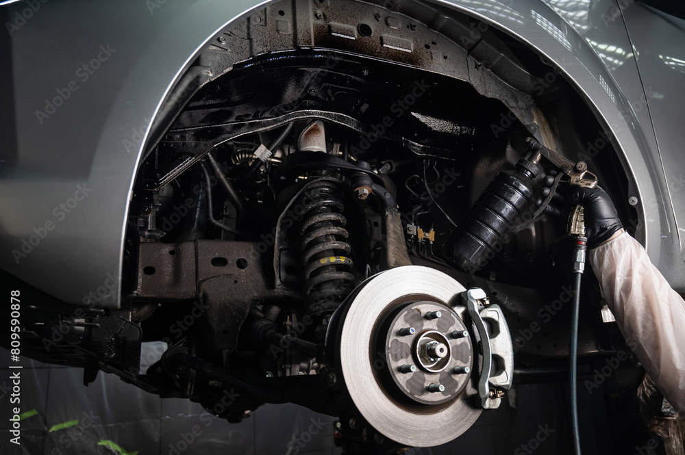 An auto mechanic applies anti-corrosion mastic to the underbody of a car. An auto mechanic applies anti-corrosion mastic to the underbody of a car.