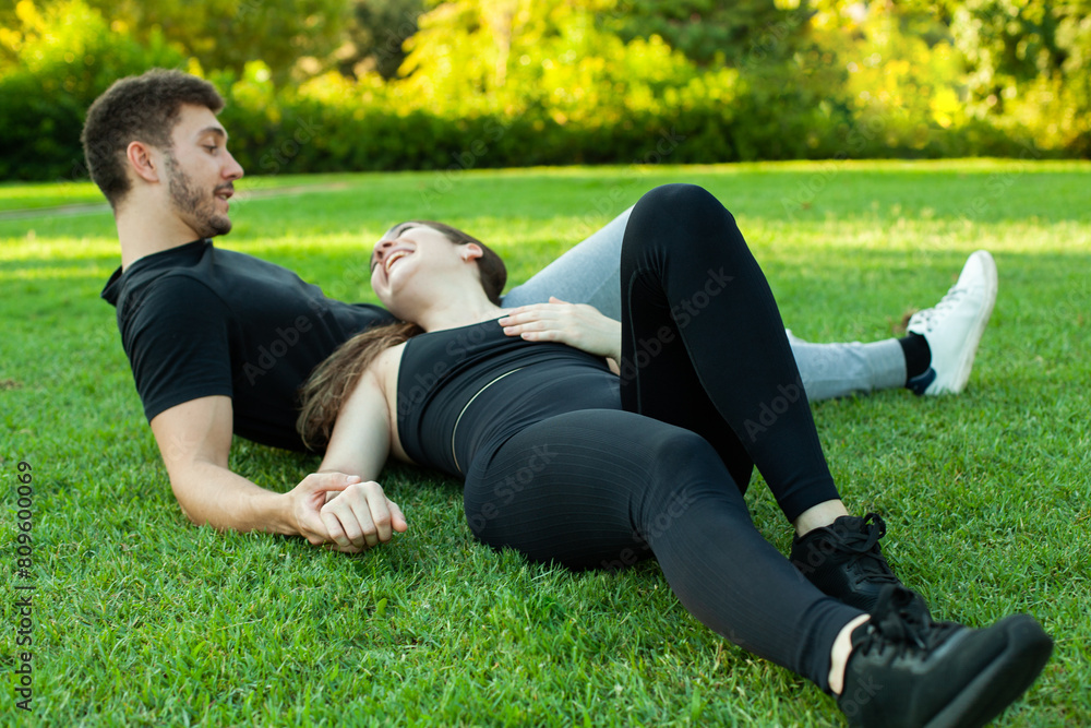 Pareja enamorada tumbada en el cesped de un parque. Deportistas descansando. Amor. Hombre y mujer mirándose Pareja enamorada tumbada en el cesped de un parque. Deportistas descansando. Amor. Hombre y mujer mirándose