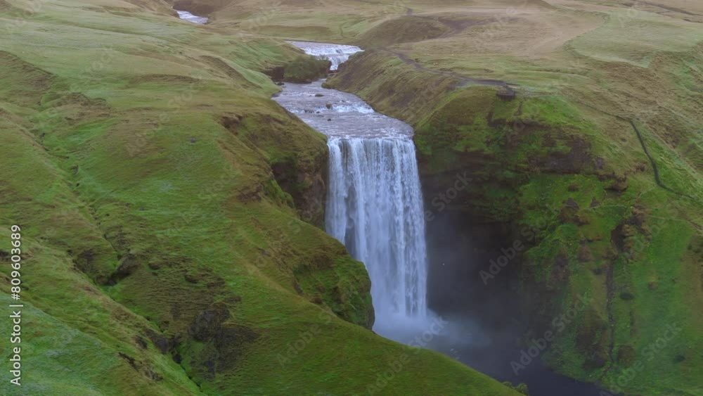 Aerial parallax perspective shows the stunning Skogafoss waterfall dramatically cutting through lush Icelandic hills, embodying the raw, unspoiled beauty of the landscape. at sunrise, Iceland, Skogar Aerial parallax perspective shows the stunning Skogafoss waterfall dramatically cutting through lush Icelandic hills, embodying the raw, unspoiled beauty of the landscape. at sunrise, Iceland, Skogar