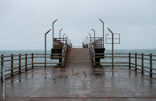 Empty pier extends into sea under grey sky, reflecting serene and moody atmosphere on rainy day.