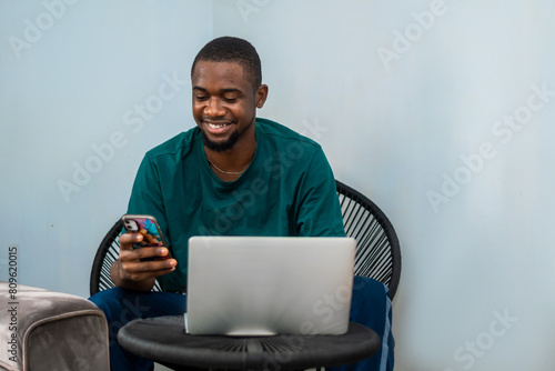Photography photo of young African American guy working on laptop and using smartphone