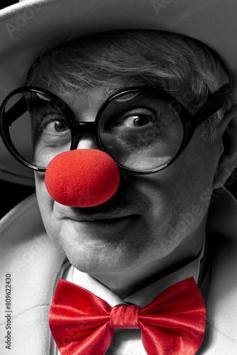 Close-up selective color portrait of a clown. An elderly man in a white coat and hat.