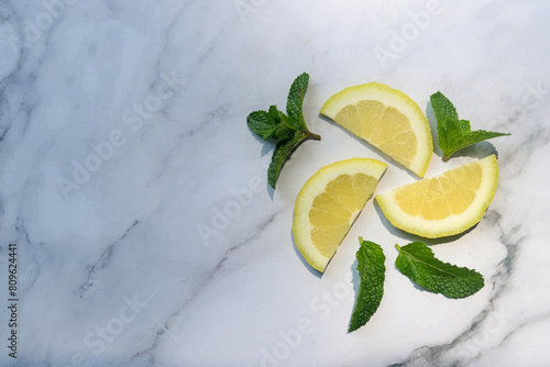 slice of organic lemon with fresh mint leaves on white marble table background.