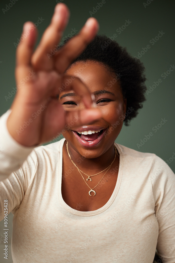 Okay sign, eye and black woman portrait in studio with smile for approval, attitude or happy on green background. Face, lady or beauty influencer with emoji finger for social media or gesture Okay sign, eye and black woman portrait in studio with smile for approval, attitude or happy on green background. Face, lady or beauty influencer with emoji finger for social media or gesture