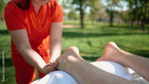 A master masseur in a bright orange uniform gives a healing body massage to a handsome man with muscles. Sports, recreation, health, relaxation and self-care in the summer outdoors photo