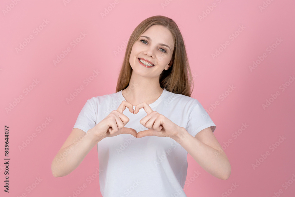 Attractive caucasian young blonde woman in casual white t-shirt looking at camera, sincerely smiling and showing heart shape gesture isolated on pink studio background. Love, feel. Attractive caucasian young blonde woman in casual white t-shirt looking at camera, sincerely smiling and showing heart shape gesture isolated on pink studio background. Love, feel.