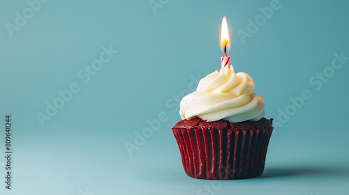 a birthday red velvet cupcake with birthday candle burning on a blue background