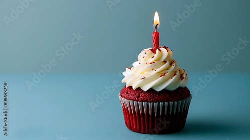 a birthday red velvet cupcake with birthday candle burning on a blue background