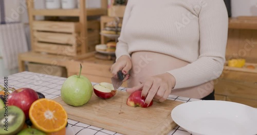 Young pregnant woman preparing fruit at kitchen in home. 4kvideo photo