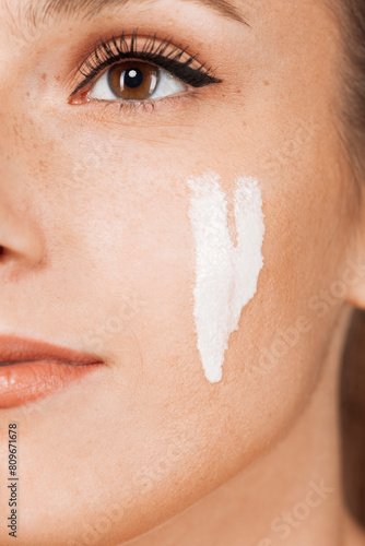 Cropped young beautiful woman with healthy skin taking care of face with cream isolated on gray background. Close up portrait. photo