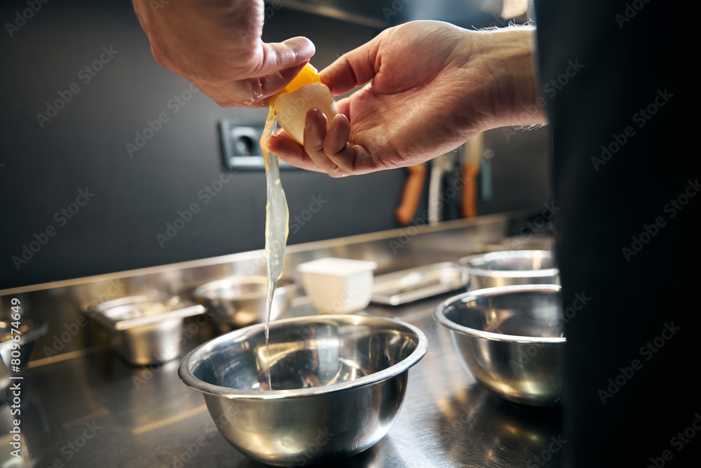 Cropped man breaking egg in bowl in modern restaurant