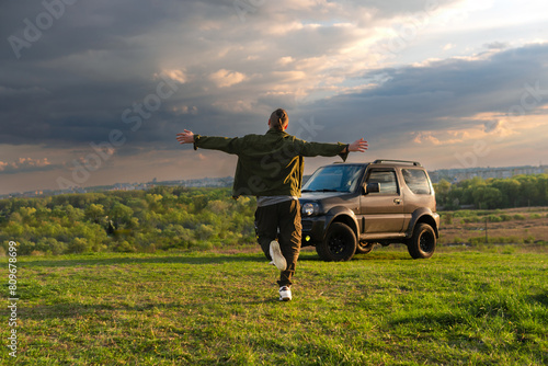 a happy man is running towards adventure on his off-road vehicle. Hands spread to the sides. The concept of active lifestyle and vacation road trip. A travelling by car to wilderness.