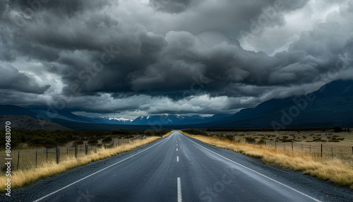 straight asphalt road going into mountains on he horizon, heavy dark clouds above mountains