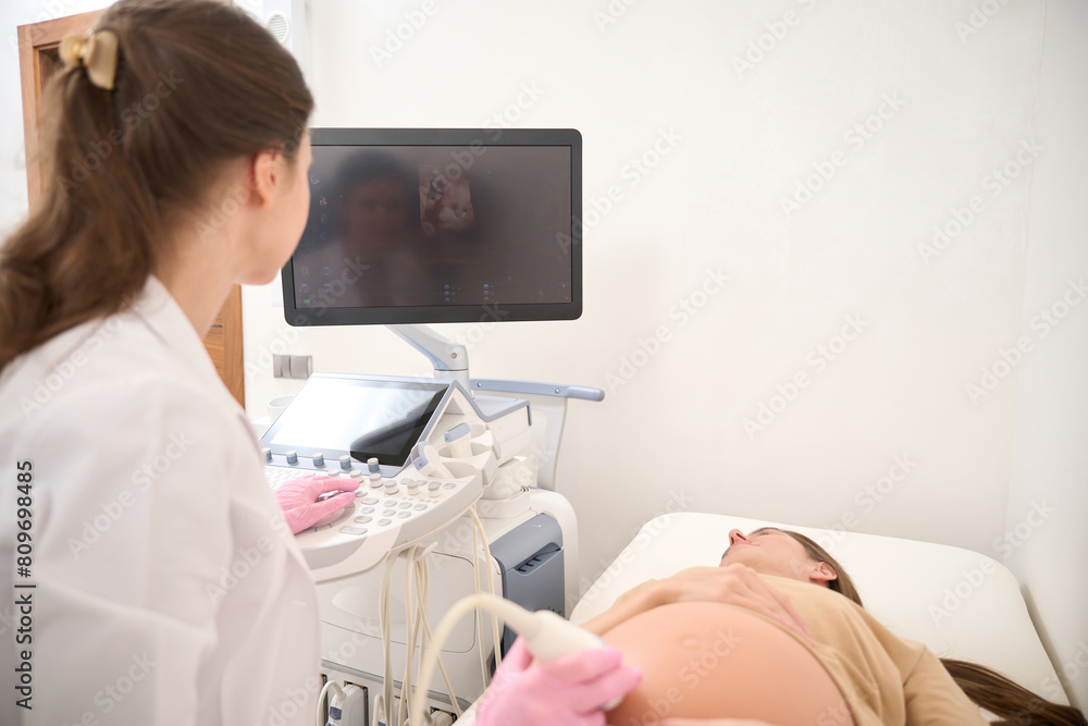 Female gynecologist doing ultrasound scanning of pregnant belly of young woman Female gynecologist doing ultrasound scanning of pregnant belly of young woman