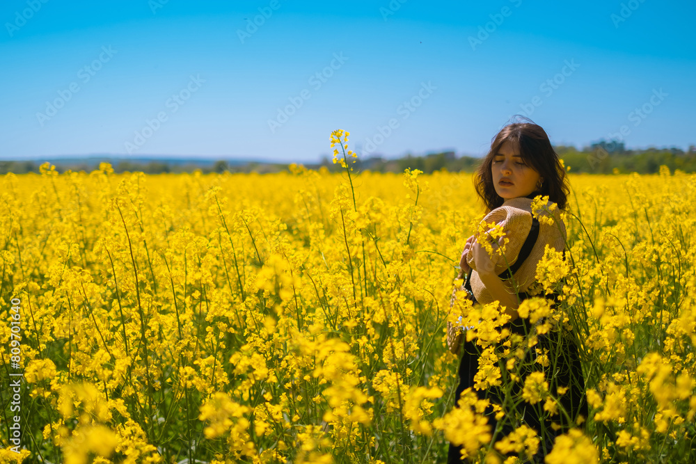 Brunette girl in straw hat, enjoying the view of blooming rapeseed field in background, embracing the beauty of nature. Brunette girl in straw hat, enjoying the view of blooming rapeseed field in background, embracing the beauty of nature.