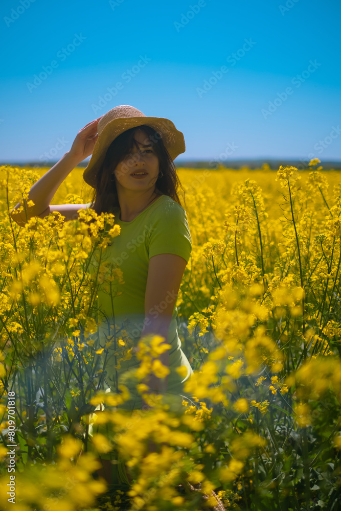 Portrait of beautiful woman in green dress, straw hat, with blooming yellow rapeseed field in background. Nature relaxation, style, and aesthetic. Portrait of beautiful woman in green dress, straw hat, with blooming yellow rapeseed field in background. Nature relaxation, style, and aesthetic.