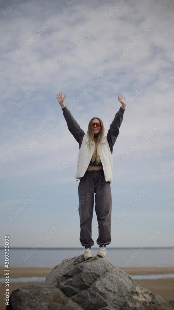 Joyous Woman with Arms Raised Standing on Rocky Beach, Exuberant Celebration, Clear Sky