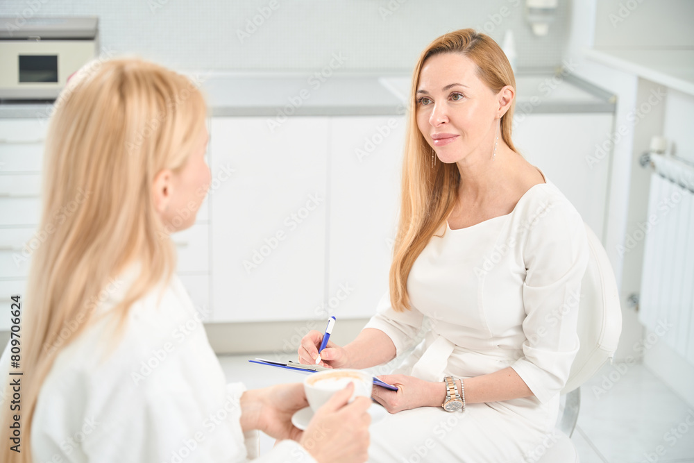 Fototapeta premium Beautiful woman therapist filling medical card of patient