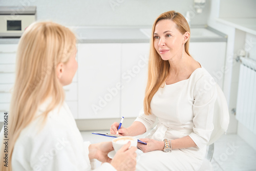 Beautiful woman therapist filling medical card of patient