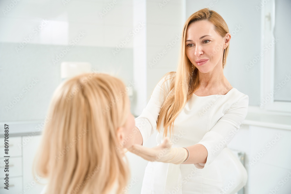 Cosmetician looking at face of female client to find imperfects of skin Cosmetician looking at face of female client to find imperfects of skin