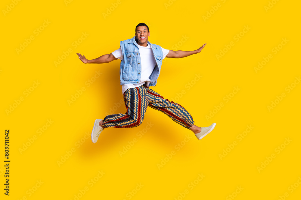 Full length photo of funky nice guy dressed jeans waistcoat print pants fly hold hands like wings isolated on yellow color background
